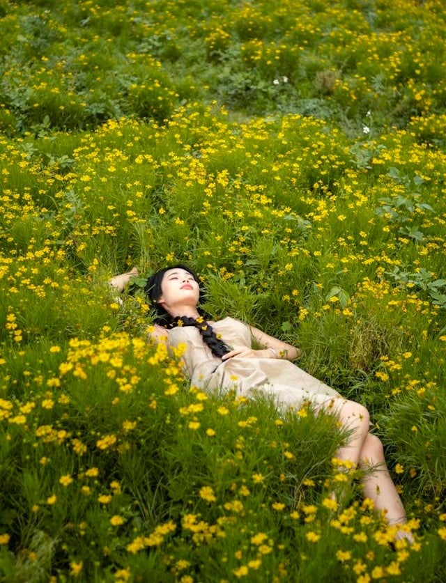 黄色い花の咲く草原で昼寝をする女性
